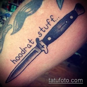 Фото тату ножа с надписью 'hoodrat stuff...' на руке. Необычный и вызывающий рисунок татуировки.