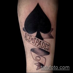 Фото тату туза пик на предплечье. Черно-белый рисунок с надписью 'Ace of Spades' на ленте. Традиционный стиль татуировки.