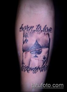 Фото татуировки на руке с изображением пики и надписи "Born to lose, live to win". Черно-белый рисунок татуировки в реалистичном стиле.