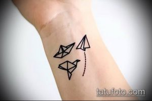 Фото тату, включающего в себя изображения оригами-лодки, самолета и птицы, расположенных на запястье.