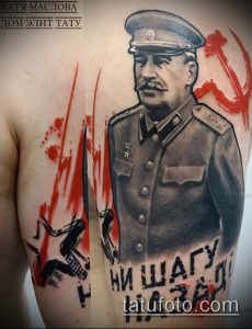 Фото тату на плече с изображением Сталина в военной форме и красным серпом и молотом. Динамичный рисунок с брызгами краски, выполненный в смешанном стиле.