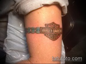 Фото тату логотипа Harley-Davidson на руке. Цветной рисунок татуировки с детальной проработкой элементов логотипа.