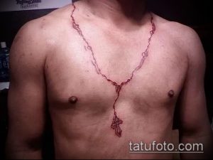 Татуировка в виде четков, выполненная красными чернилами на груди мужчины. Четки ниспадают по груди, заканчиваясь крестом. Необычный и привлекающий внимание дизайн.