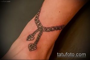 Татуировка в виде цепи с двумя висящими замками на запястье. Тату выполнено в серо-черных тонах, с детализированной прорисовкой звеньев цепи и замков.