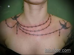 Фото тату: женственная татуировка в виде ожерелья с подвесками-ласточками на шее и ключицах. Черно-серый рисунок татуировки.