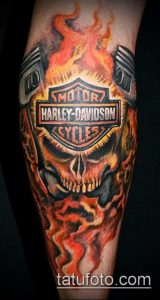 Фото тату: череп с логотипом Harley-Davidson, окруженный пламенем. Реалистичная проработка деталей и яркие цвета.