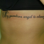 Фото татуировки надписи "My guardian angel is always with me" на боку, выполненной каллиграфическим шрифтом.