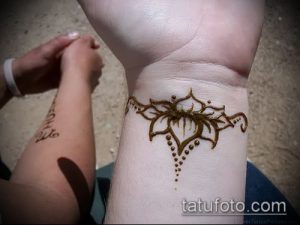 Фото тату хной на запястье: стилизованный цветок с тонкими линиями и точками, выполненный в коричневых тонах.