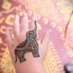 Фото тату слона на ладони в стиле мехенди. Детализированный рисунок с использованием темных оттенков и сложных узоров.