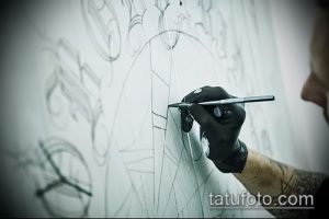 Фото мастера тату, рисующего эскиз татуировки на бумаге. Рука мастера с татуировкой держит карандаш, создавая сложный рисунок.