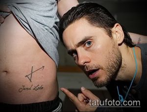 Фото тату Джареда Лето: небольшая татуировка со стрелкой и надписью 'Jared Leto' на животе. Персонализированный и значимый эскиз татуировки.