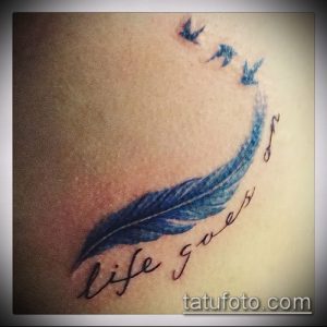 Фото тату: перо, из которого вылетают птицы, и надпись "Life goes on", выполненные в синих тонах на коже.