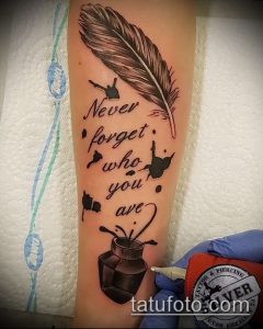 Фото тату на предплечье с изображением пера, чернильницы и надписи 'Never forget who you are'. Красивый рисунок татуировки с глубоким смыслом.