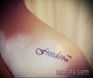 Фото тату на ключице с надписью "Freedom" выполненной красивым шрифтом и украшенной маленькими птицами.