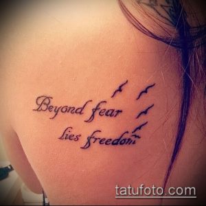 Фото тату на плече с надписью "Beyond fear lies freedom" и изображением нескольких летящих птиц. Рисунок выполнен в тонких линиях.