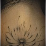 Фото тату: минималистичный эскиз лотоса в технике blackwork, расположенный на задней части шеи. Нежные линии и плавные переходы создают элегантный образ.
