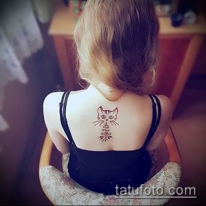 Фото тату: небольшая татуировка кошки, выполненная хной, на спине девушки. Рисунок простой и милый, с использованием коричневых оттенков.