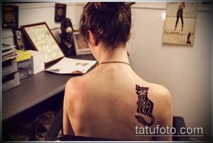 Фото тату: черная татуировка кошки на лопатке девушки. Минималистичный рисунок с плавными линиями и акцентом на грациозность.