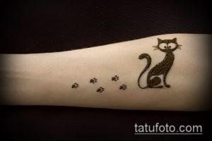 Фото тату коричневой кошки, сидящей на руке и оставляющей за собой отпечатки лап. Нежный и очаровательный рисунок татуировки.