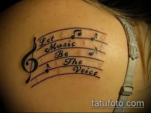 Фото тату на лопатке: музыкальные ноты и фраза 'Let Music Be The Voice' выполнены в черном цвете.