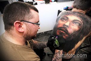 Фото тату: мастер татуировки делает татуировку Иисуса Христа на спине клиента, используя тату-машинку.