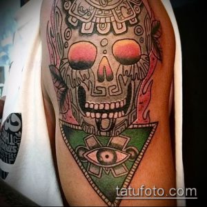 Фото тату черепа в ярком стиле traditional tattoo. Череп украшен геометрическими узорами и символами, а вокруг него видны языки пламени.