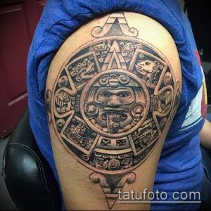 Фото тату ацтекского календаря на плече, выполненного в технике blackwork. Детализированный рисунок с геометрическими узорами и символами древней цивилизации.