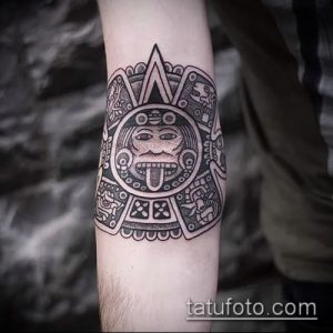 Фото тату календаря ацтеков на локтевом суставе, выполненное в технике blackwork. Детализированный рисунок с изображением лица в центре.