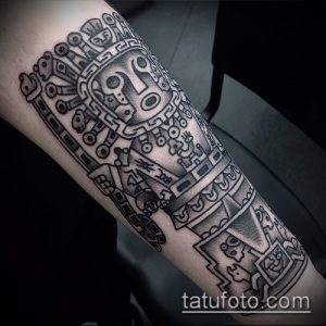 Фото тату в стиле ацтекских узоров на предплечье, выполненное в технике blackwork. Длинный рисунок с изображением различных символов и фигур.