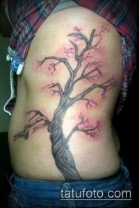 Фото тату цветущей сакуры на боку женщины. Нежные розовые цветы и детально проработанный ствол дерева создают гармоничный рисунок.