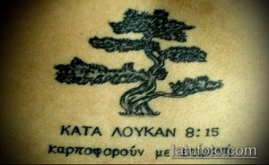 Фото тату дерева в черно-белом исполнении с греческой надписью под ним. Минималистичный рисунок татуировки.