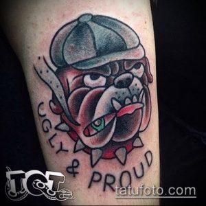 Фото тату: бульдог в кепке, надпись "Ugly & Proud", традиционный стиль, шипы на ошейнике. Идеи для тату на руке.