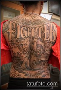 Фото татуировки на всю спину с изображением масок, надписи 'FIGHTER' и элементов мексиканской культуры. Черно-серый рисунок.