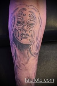 Фото тату девушки в стиле сахарной черепушки (Santa Muerte) на руке. Черно-серые тона, детализированный макияж, цветы и узоры.