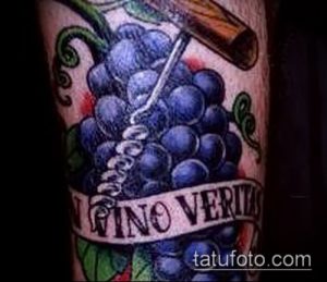 Фото татуировки на руке с изображением грозди винограда, штопора и надписи 'Vino Veritas'. Яркий и детализированный рисунок.