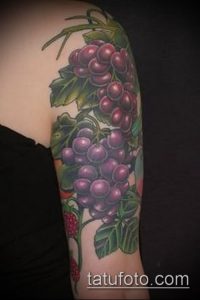 Фото татуировки на предплечье с изображением грозди винограда, клубники и зеленых листьев. Яркие цвета и реалистичный рисунок.