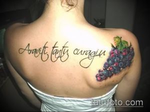 Фото тату: гроздь фиолетового винограда и латинская надпись "Amor, tantus cruciatus" на спине девушки. Детализированный рисунок татуировки.