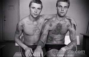 Фотография двух мужчин с тюремными татуировками на теле. Видны рисунки на груди, плечах и руках, выполненные в традиционном стиле.