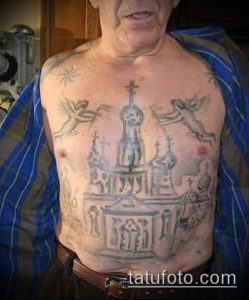 Фото татуировки церкви с ангелами на теле пожилого мужчины. Черно-серый рисунок татуировки, выполненный в реалистичном стиле. Фотография сделана в помещении.