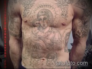 Фото татуировки Богоматери с младенцем Иисусом на груди мужчины. Черно-серый рисунок татуировки, выполненный в реалистичном стиле. Фотография сделана в помещении.