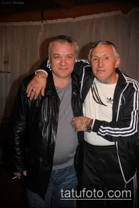 Фотография двух мужчин, предположительно известных мастеров тату, обнимающихся и позирующих для камеры. На руках у них видны татуировки.