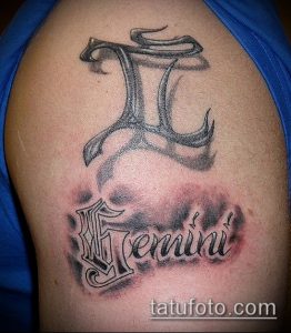 Фото тату на плече: изображение знака зодиака Близнецы с именем 'Gemini'. Использованы черные и серые оттенки, создающие объемный эффект.