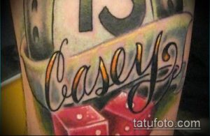 Фото тату с надписью 'Casey' и двумя красными игральными костями на руке. Классический рисунок татуировки с использованием ярких цветов.