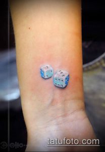 Фото миниатюрной татуировки на запястье с изображением двух голубых игральных костей.