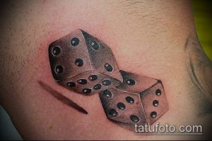 Фотография реалистичной татуировки с двумя игральными костями, расположенными на плече. Детализированный рисунок татуировки с использованием светотени.