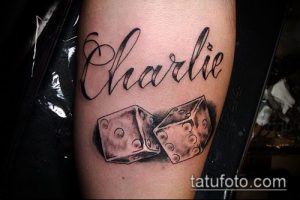 Фото тату: татуировка на руке с изображением имени "Charlie" в красивом каллиграфическом стиле и двух игральных костей. Рисунок татуировки выполнен в черно-белой гамме.