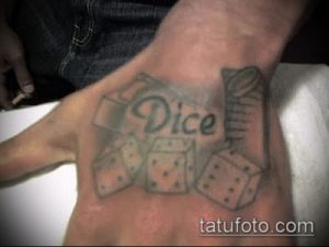 Фото тату на руке с изображением игральных костей и надписи 'Dice'. Черно-белый рисунок татуировки в простом стиле.