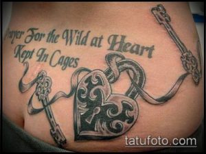 Фото тату замка и ключа на животе с надписью 'Pray For the Wild at Heart Kept In Cages'. Черно-серый рисунок татуировки в реалистичном стиле.