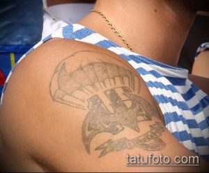 Фото старой татуировки логотипа Бэтмена на плече. Черно-серый рисунок с размытыми контурами, свидетельствующий о времени.