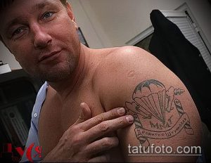 Фото татуировки на плече с изображением раскрытого парашюта и надписи "Десантные крылатые". Черно-серые тона, реалистичный стиль, детализированная проработка.